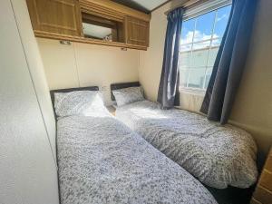 Duas camas num pequeno quarto com uma janela em Great 4 Berth Caravan For Hire In Suffolk At North Denes, Ref 40149nd em Lowestoft