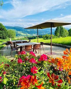 un patio con mesas y sillas bajo una sombrilla en Alpenloge Boutique Hotel en Scheidegg