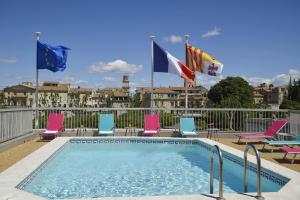 een zwembad met roze en blauwe stoelen en vlaggen bij Hôtel Atrium in Arles