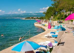 ein Strand mit Stühlen und Sonnenschirmen und Menschen im Wasser in der Unterkunft App2 Marin in Šilo