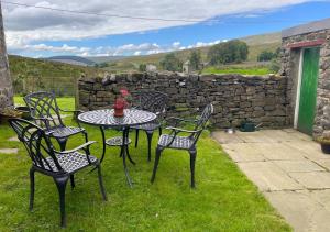 a table and chairs on the grass with a stone wall at Moorland View in Cotterdale