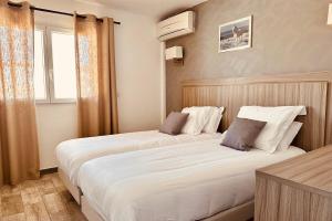 two beds in a hotel room with a window at Hotel Les Palmiers En Camargue in Saintes-Maries-de-la-Mer