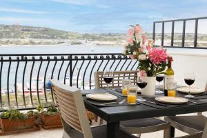 a table with wine glasses and flowers on a balcony at Ghadirabay Seafront With Sea Views By Homely in Mellieħa