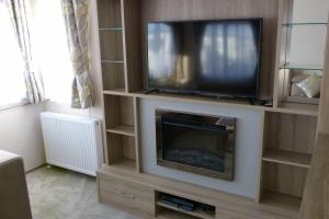a entertainment center with a tv and a fireplace at SBL38 Caravan at Camber Sands - quiet location in Camber