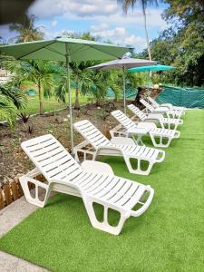 a row of white lounge chairs and an umbrella at Bungalow charmant au Moule avec piscine et jardin in Le Moule