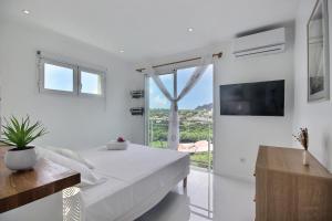 a white bedroom with a bed and a large window at Villa Linay in Le Diamant