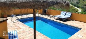 a swimming pool with two chairs and an umbrella at Los Montes Traditional Casa with private pool in Viñuela