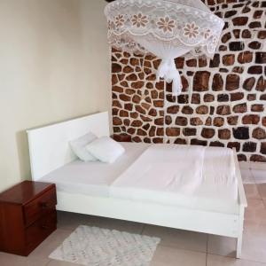 Cama blanca en habitación con pared de ladrillo en COLIBRI Saint Joseph de Sabel, en Gisenyi