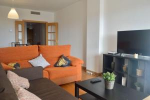 a living room with an orange couch and a flat screen tv at Teatinos Atico Penthouse Pool WiFi Parking in Málaga