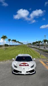 a white car parked on a road next to a field at Red Dragon Okinawa #Welcome! 欢迎! ยินดีต้อนรับ #貸切価格 chartering a whole building #Presidential Suite Villa #Great access to all locations #Easy money exchange #LibertyWalk Supercar ヨット クルーザー オーナー 御用達 #世界遺産 #各所アクセス最高 in Minatogawa