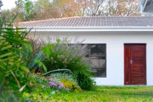 Pemabwe Guest Lodge في هراري: بيت ابيض بباب احمر وبعض النباتات