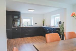 a kitchen with black cabinets and orange chairs at Tegelvillan på golfbanan in Oxie