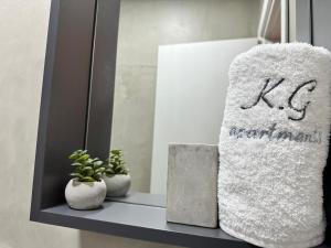 une serviette blanche assise sur une étagère avec deux plantes dans l'établissement K.G APARTMENT 2, à Pefkohori