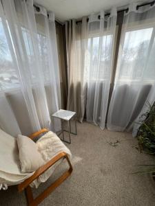 Habitación con cortinas blancas, silla y ventanas. en Homestay in cozy River Heights home, en Winnipeg