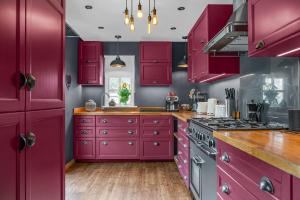 a red kitchen with purple cabinets and a stove at The Blue Anchor House - close to London in Hertford
