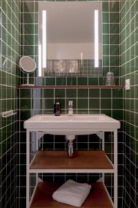Baño de azulejos verdes con lavabo y espejo en Hôtel Les Beaux Arts, en Compiègne