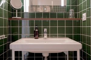 a white sink in a green tiled bathroom at Hôtel Les Beaux Arts in Compiègne