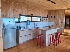 a kitchen with a white refrigerator and red bar stools at Casa Bosquemar Boyeruca in Vichuquén