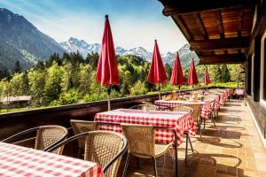 a row of tables with red umbrellas on a balcony with mountains at Alpengasthof Hotel Schwand in Oberstdorf