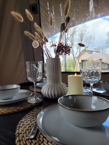 a table with plates and glasses and a vase with flowers at Glampinglodge 2 pers met hottub in Meerssen