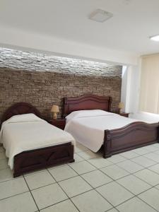 HOTEL PUERTA DEL SOL في سانتو دومينغو دا لوس كولورادوس: غرفة نوم بسريرين وجدار من الطوب