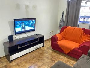 - un salon avec une télévision et un canapé rouge dans l'établissement Pé na areia praia da Guilhermina II, à Praia Grande