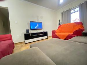 - un salon avec deux chaises rouges et une télévision à écran plat dans l'établissement Pé na areia praia da Guilhermina II, à Praia Grande