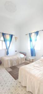 two beds in a white room with blue curtains at Villa chez NADA in Essaouira