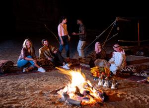 un gruppo di persone seduti intorno al fuoco sulla spiaggia di Campsite for Stays, Event Parties, holidays with Foods and Entertainments a Dubai
