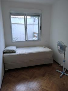 Cama en habitación con ventana y ventilador en Benito blanco, en Montevideo
