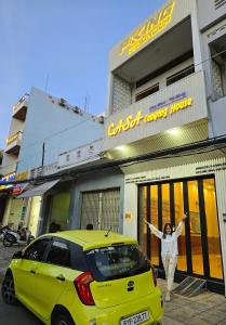 a woman standing in front of a yellow car in front of a building at CASA Camping House in Tuy Hoa