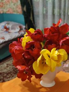 a white vase with red and yellow flowers on a table at 锦江LoveMyHome in Almaty