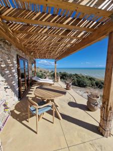 een houten tafel en een stoel op een patio met het strand bij Tendu' Punta Bianca Glamping Camp in Palma di Montechiaro