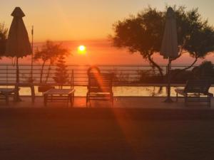 - un coucher de soleil au-dessus d'une piscine avec des chaises et des parasols dans l'établissement Molivos Sunset Apartments, à Mithimna