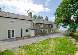 an old stone house with a windmill in the background at Cyfannedd Uchaf in Fairbourne