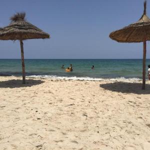 two straw umbrellas on a beach with people in the water at Appartement Cerine 1 , nur 100 Meter bis Tantana Strand in Port El Kantaoui