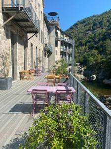 une terrasse avec des tables et des chaises roses à côté d'une rivière dans l'établissement La manufacture, à Antraigues-sur-Volane