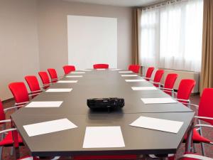 une salle de conférence avec une grande table et des chaises rouges dans l'établissement ibis Senlis, à Senlis