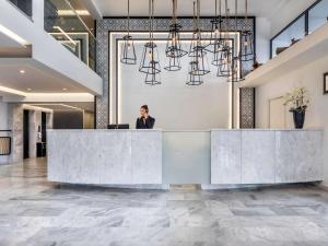 a woman standing behind a reception desk in a lobby at Mercure Rhodes Alexia Hotel & Spa in Rhodes Town