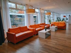 un vestíbulo con sofás naranjas, mesas y ventanas en ibis budget Berlin Ost, en Berlín