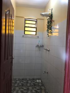 a bathroom with a shower with white tiles and a window at Kisumu Airview Homestay in Kisumu