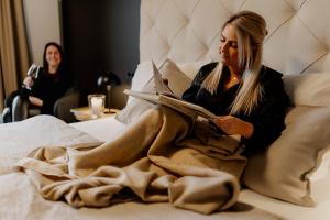 Eine Frau, die auf einem Bett sitzt und ein Buch liest. in der Unterkunft 2tHEIMAT - Hotel & Restaurant in Morbach