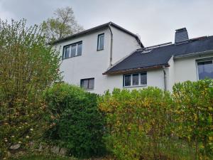 a white house with a black roof and some bushes at Ferienwohnung Erzgebirgsblick in Bernsbach