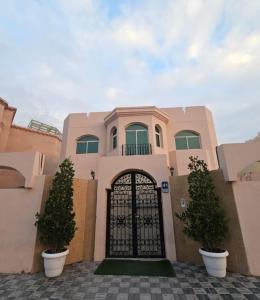 International Abu Dhabi Hostel في أبوظبي: بيت وردي فيه بوابة وشجيرتين