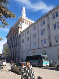 una mujer caminando frente a un edificio con un autobús en Emily House, en Fier