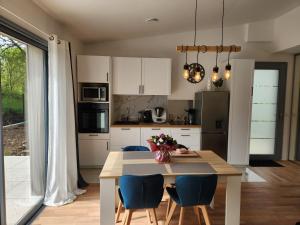 una cocina con mesa con sillas azules y una cocina con armarios blancos en La petite maison d'Adèle, en Hargeville-sur-Chée