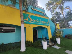 een geel en blauw gebouw met palmbomen voor de deur bij Pousada Sereia Tropical in Guarujá