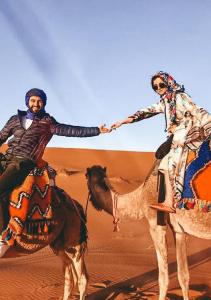 a man and a woman riding on a camel in the desert at Explore merzouga luxury camp in Merzouga