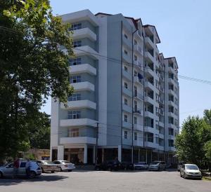 a tall white building with cars parked in a parking lot at Cozy Apartment In Old Town Kutaisi in Kutaisi