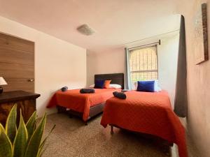 グアテマラシティにあるNoMAD Houseのベッドルーム1室(オレンジのシーツが敷かれたベッド2台、窓付)